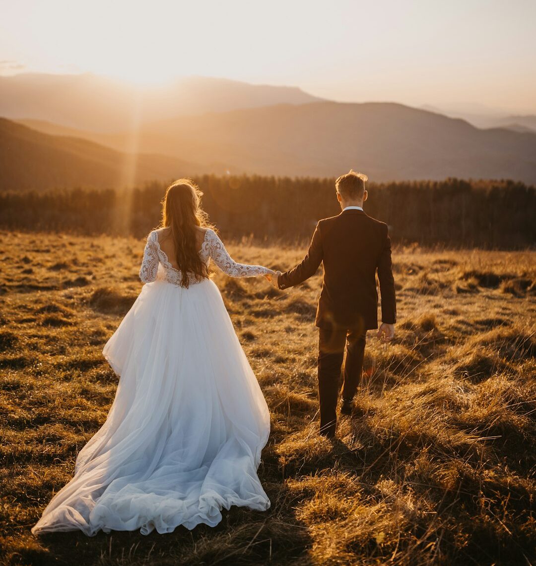 man and woman in wedding dress walking on brown grass field during daytime
